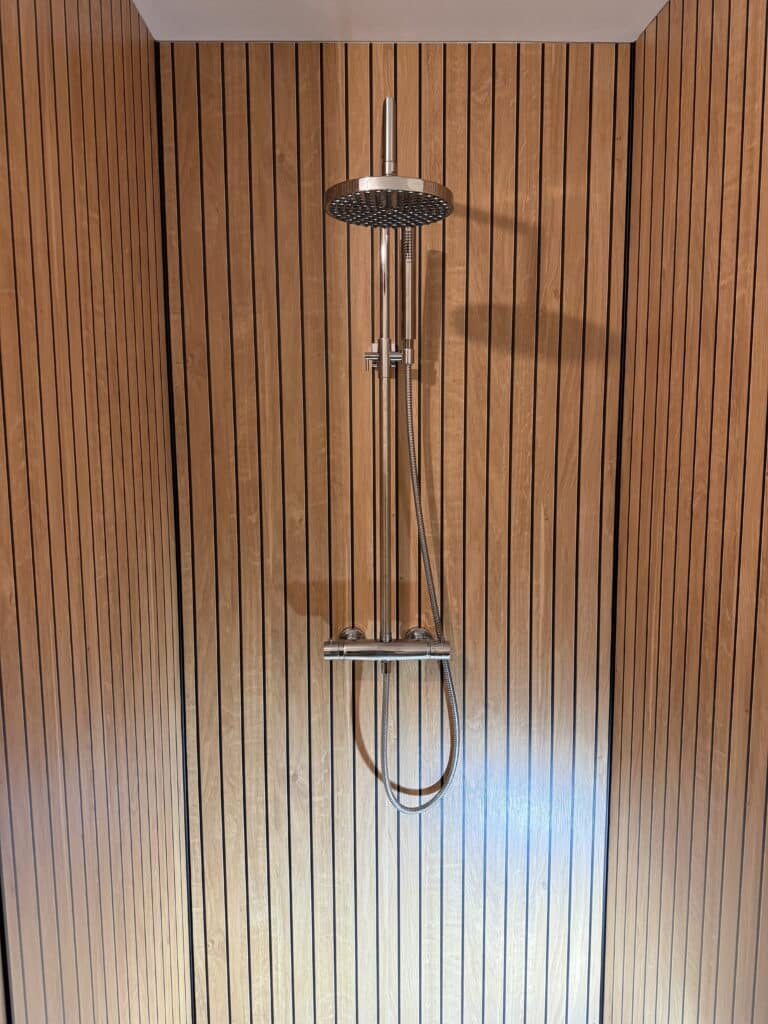 Douche Moderne sur Mur en Tasseaux de Bois | Design Zen Pommeau de douche moderne en métal brossé sur un mur en tasseaux de bois clair pour une salle de bain zen.