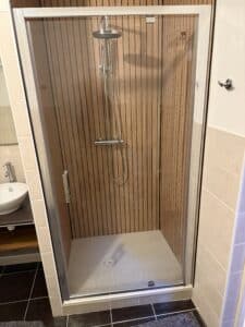 Douche moderne avec paroi en tasseaux de bois, colonne de douche chromée et porte vitrée.