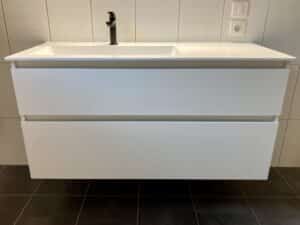 Meuble vasque blanc suspendu moderne avec robinet noir et deux tiroirs de rangement devant un mur carrelé.