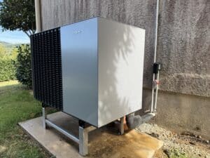 Pompe à chaleur Viessmann grise et noire installée sur un socle béton dans un jardin devant un mur crépi.