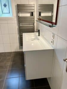 Meuble vasque blanc suspendu avec mitigeur noir et sèche-serviette design dans une salle de bain carrelée moderne.