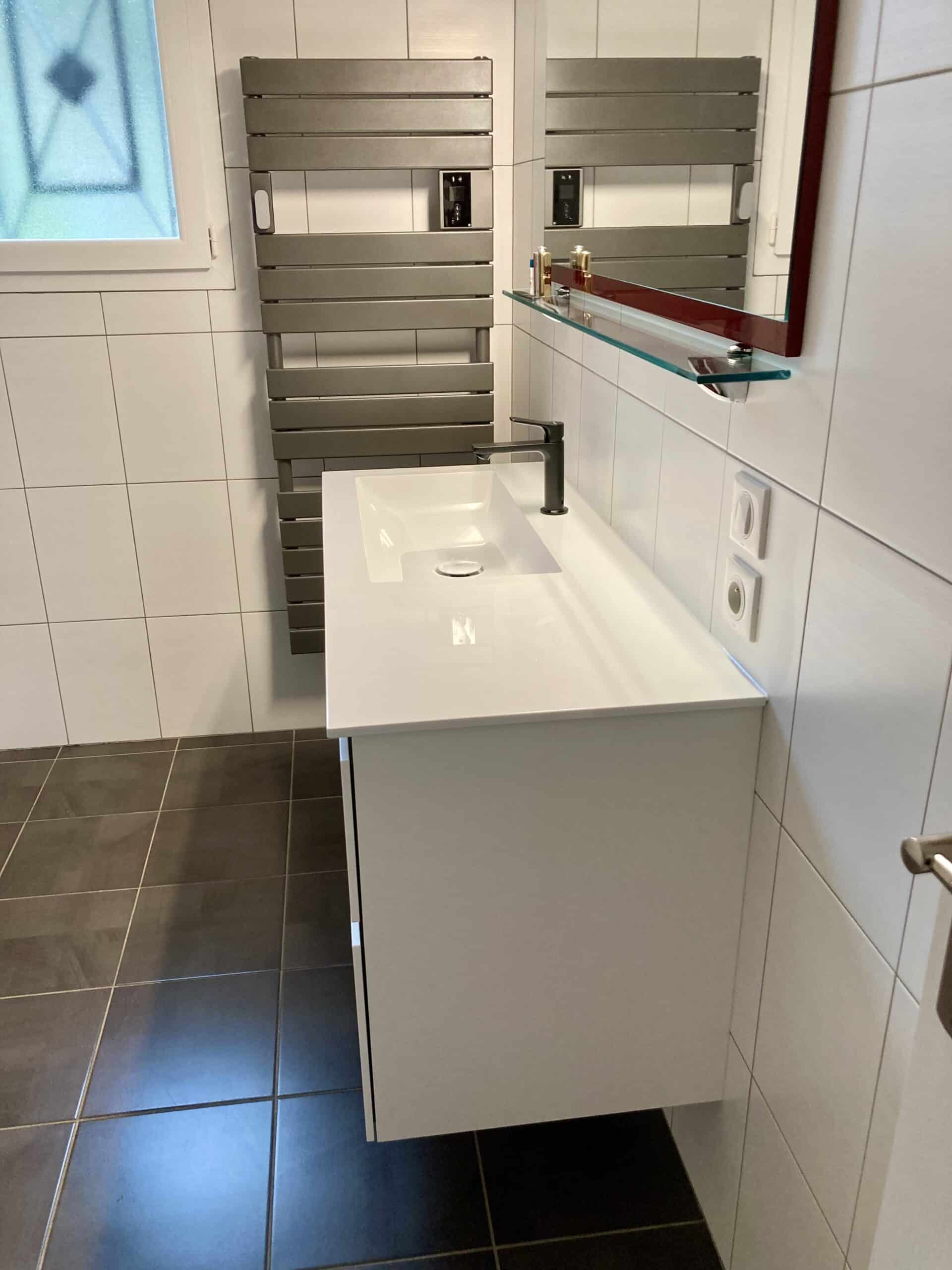 Meuble vasque blanc suspendu avec mitigeur noir et sèche-serviette design dans une salle de bain carrelée moderne.