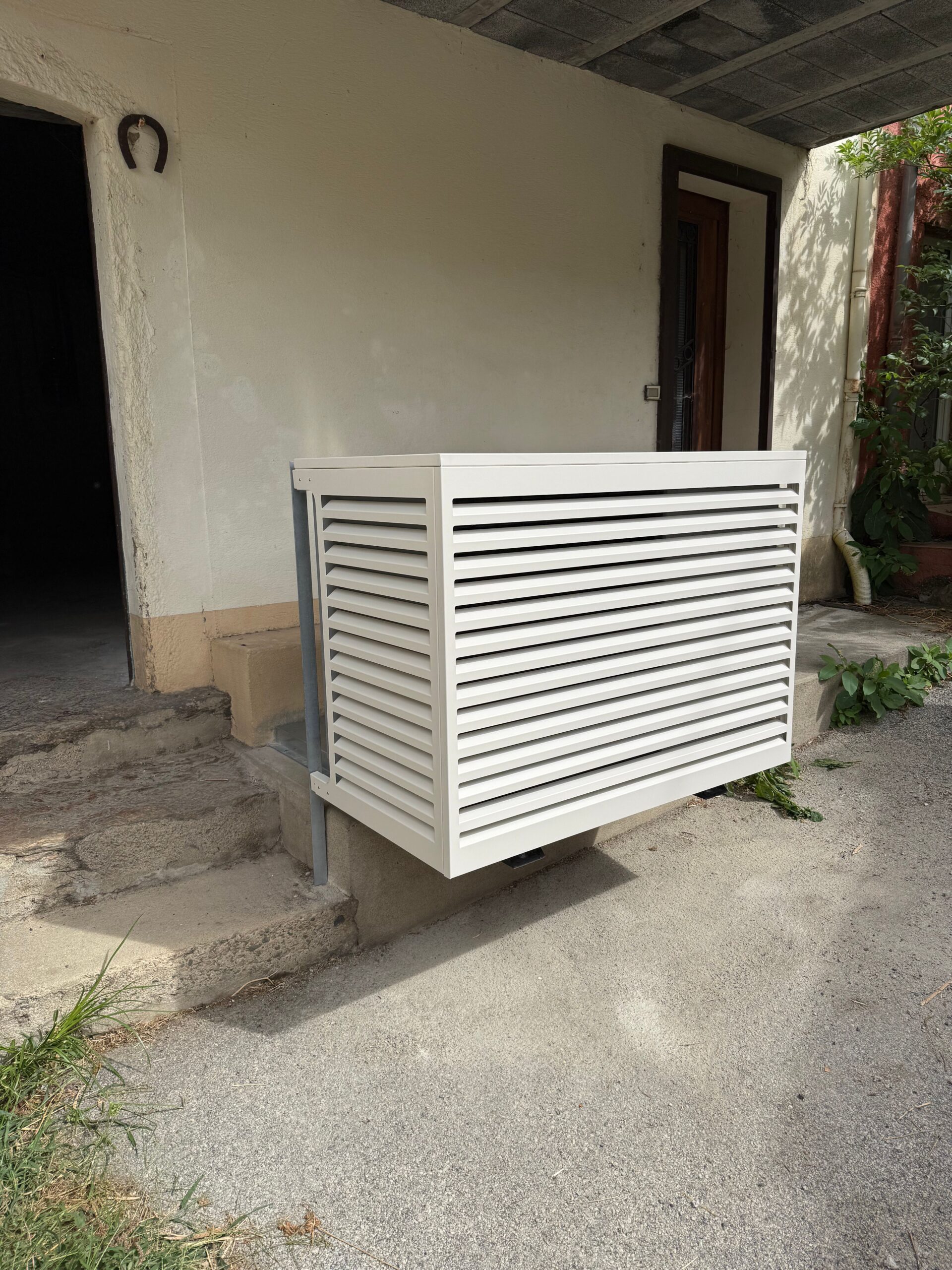 Cache-clim blanc design à persiennes devant une façade de maison.