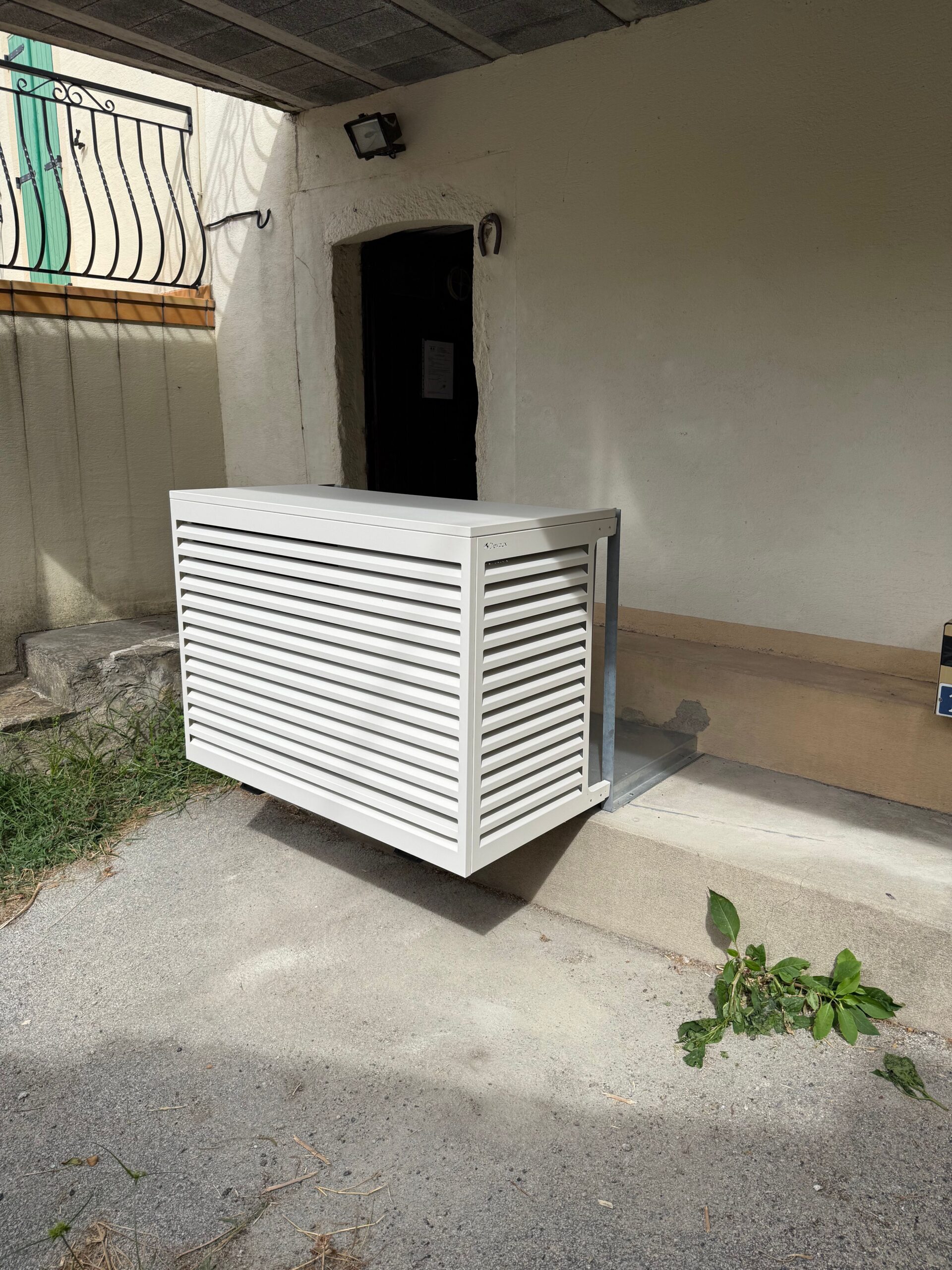 Cache-climatisation blanc Decco à persiennes installé en extérieur contre un mur.