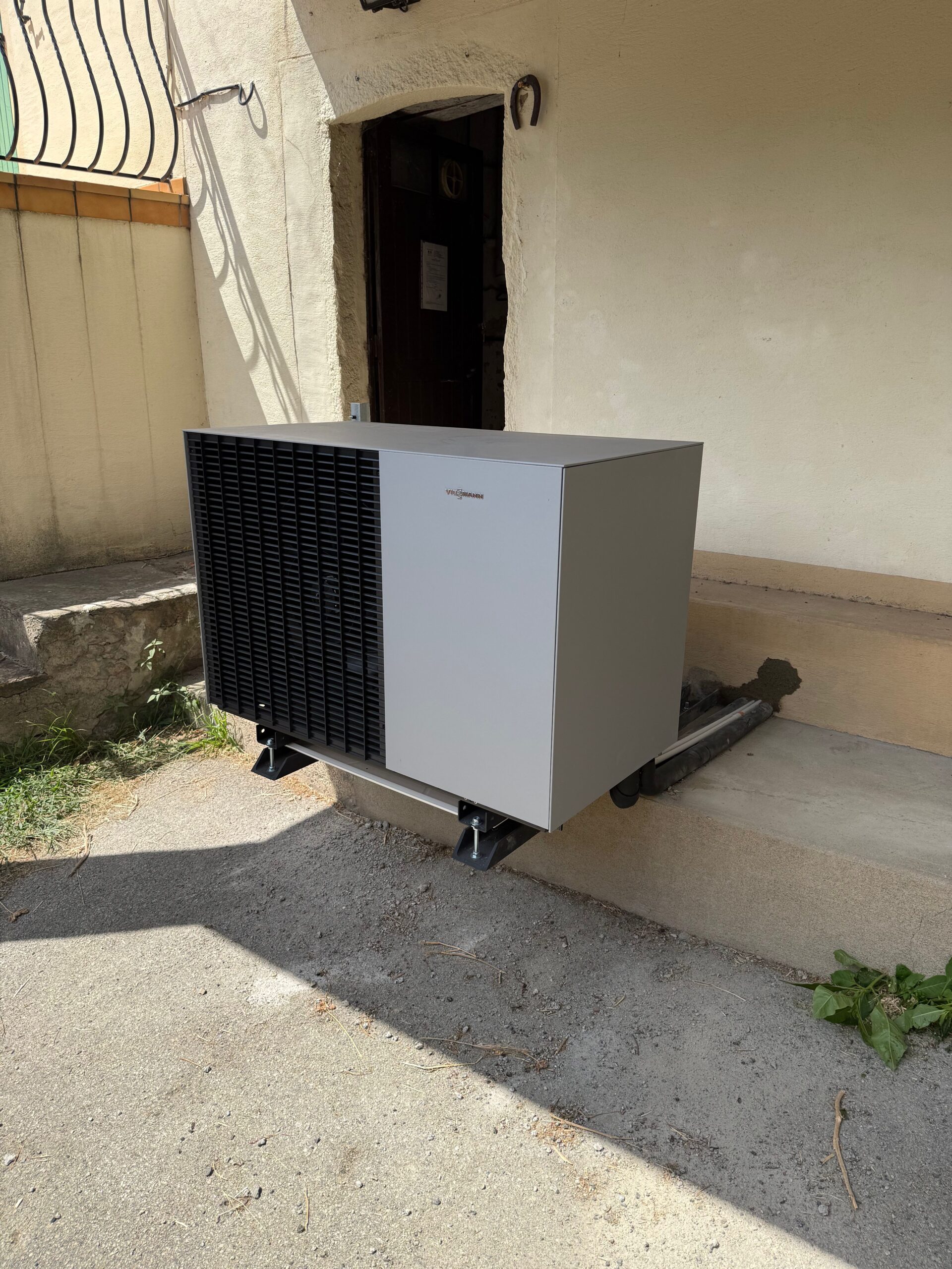Pompe à chaleur Viessmann grise installée sur supports extérieurs devant la façade d'une maison.